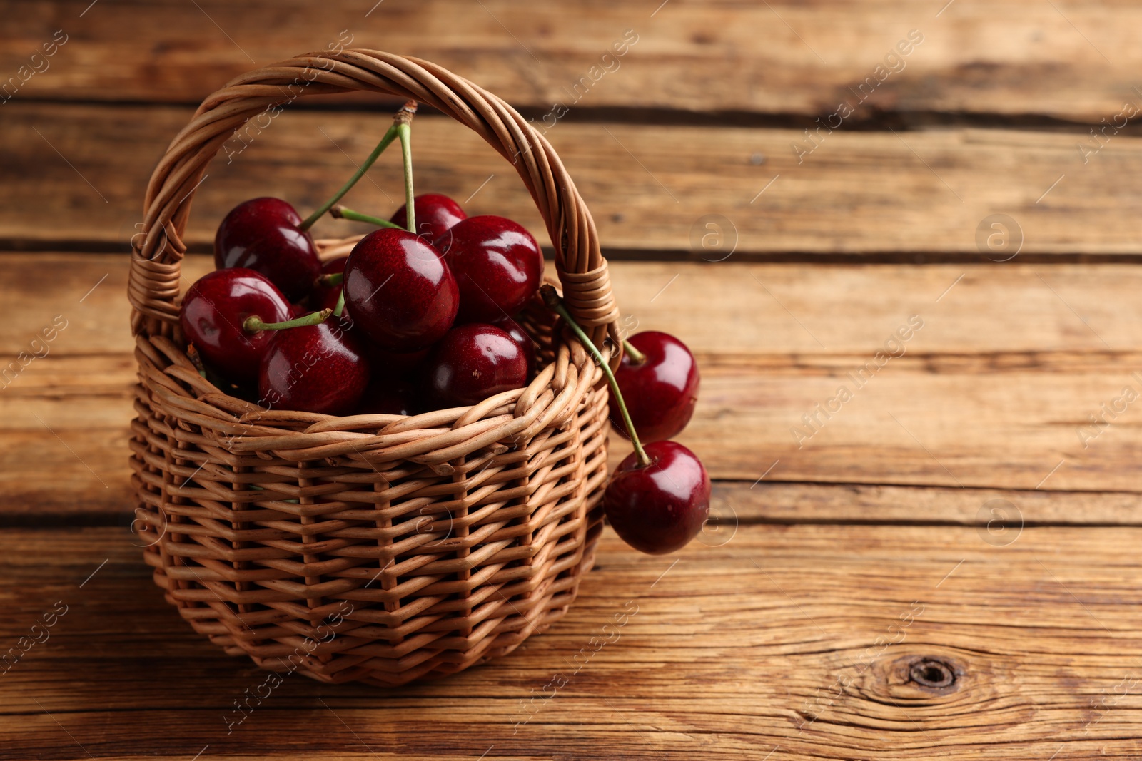 Photo of Wicker basket of ripe sweet cherries on wooden table, space for text