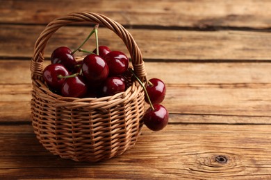 Wicker basket of ripe sweet cherries on wooden table, space for text