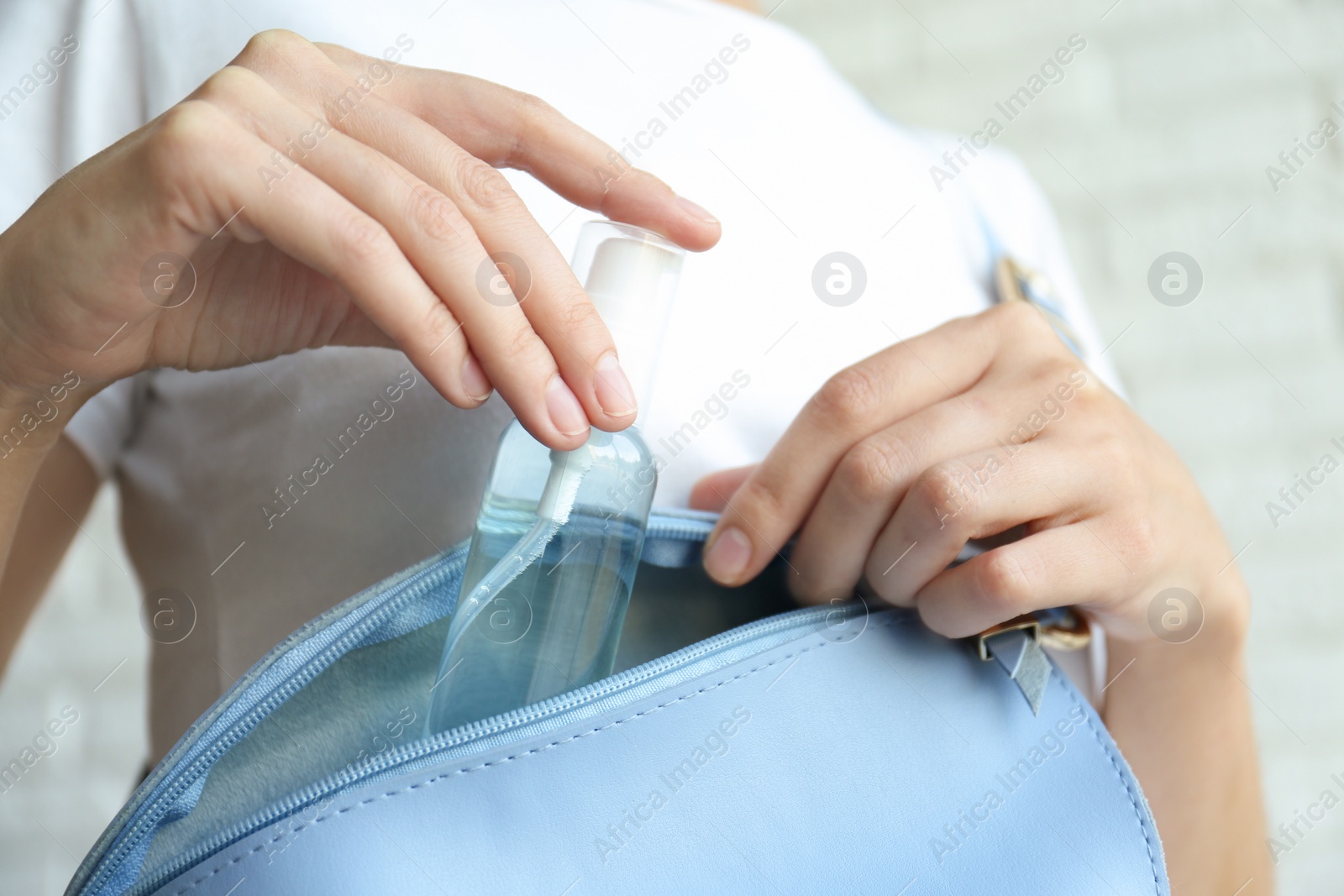 Photo of Woman putting hand sanitizer in purse on light background, closeup. Personal hygiene during COVID-19 pandemic