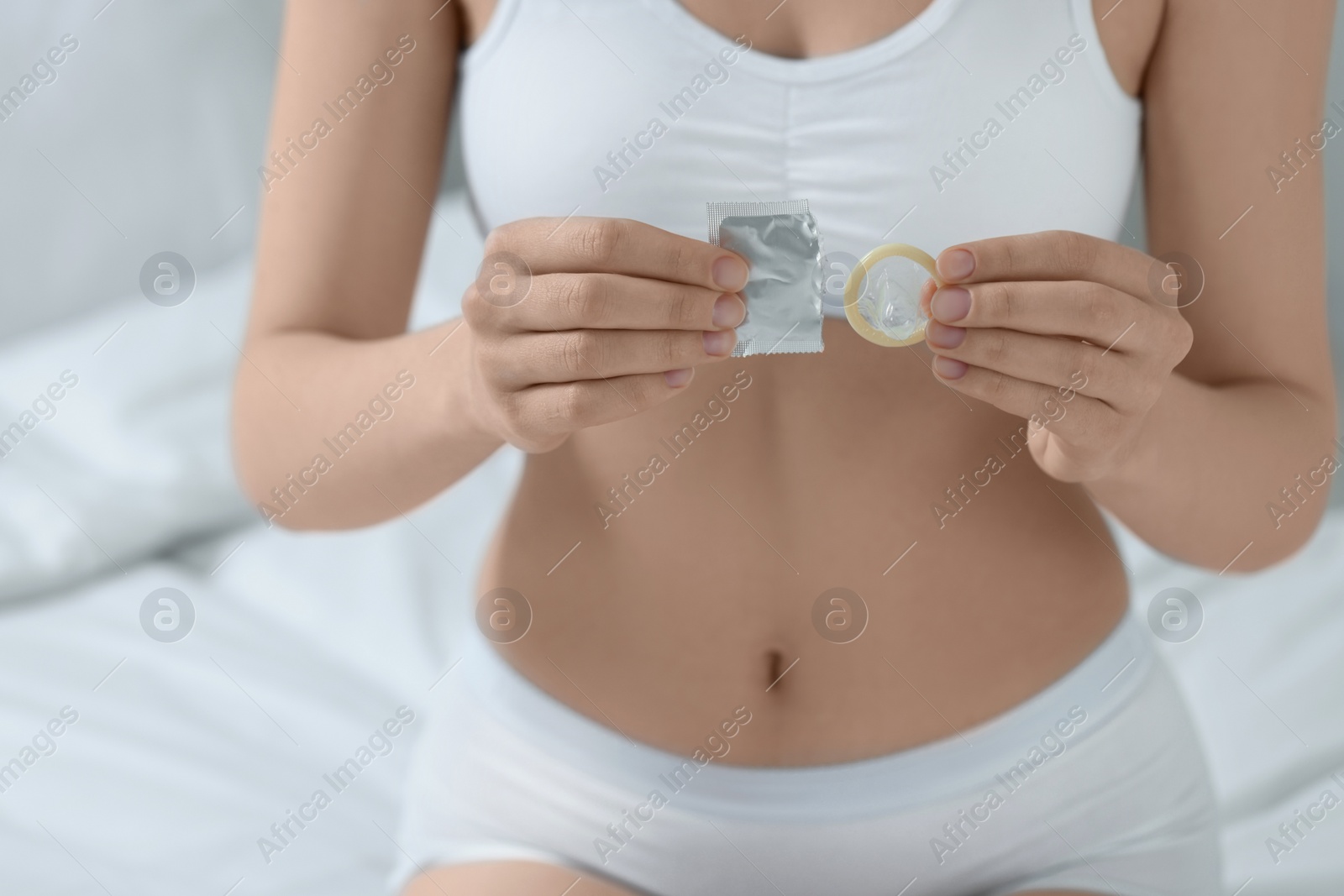 Photo of Woman holding unwrapped condom on bed indoors, closeup. Safe sex