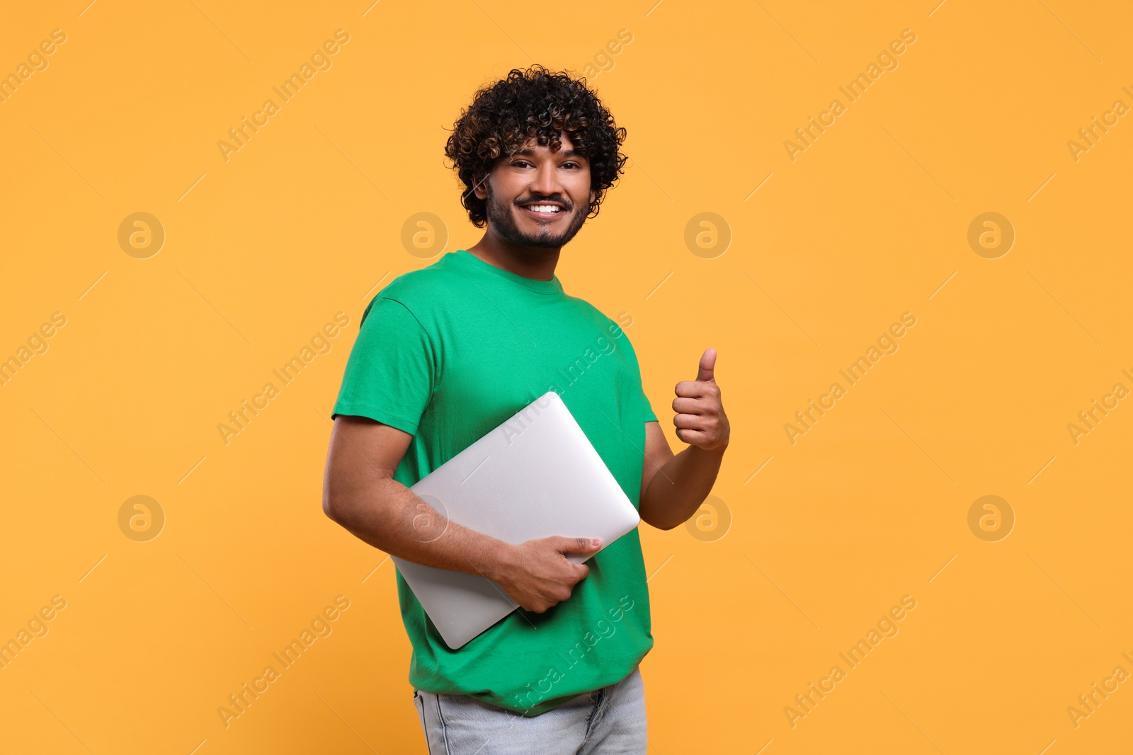 Photo of Smiling man with laptop showing thumbs up on yellow background