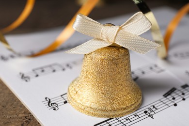 Photo of Golden bell and music sheets on wooden table, closeup. Christmas decor