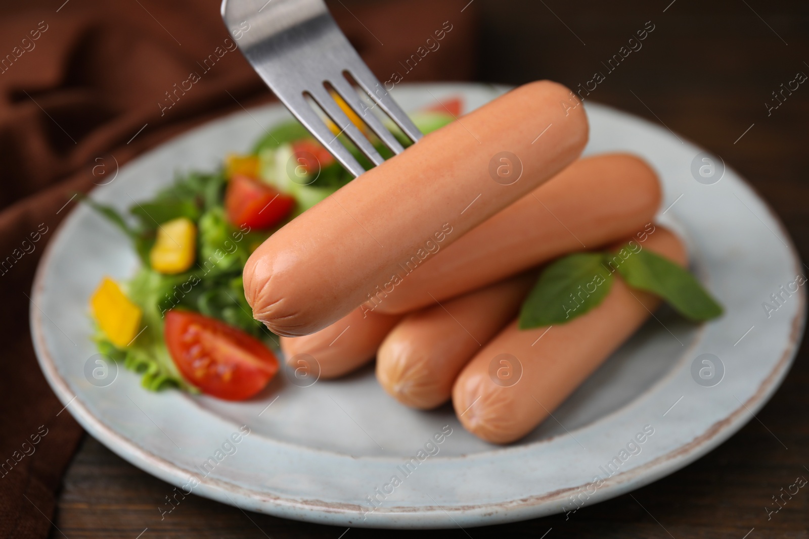 Photo of Fork with delicious boiled sausage over plate, closeup