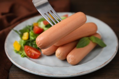 Fork with delicious boiled sausage over plate, closeup