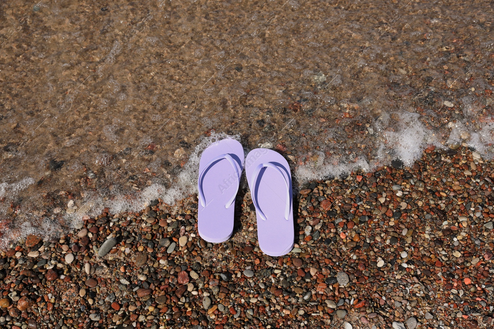 Photo of Stylish violet flip flops on beach pebbles, top view