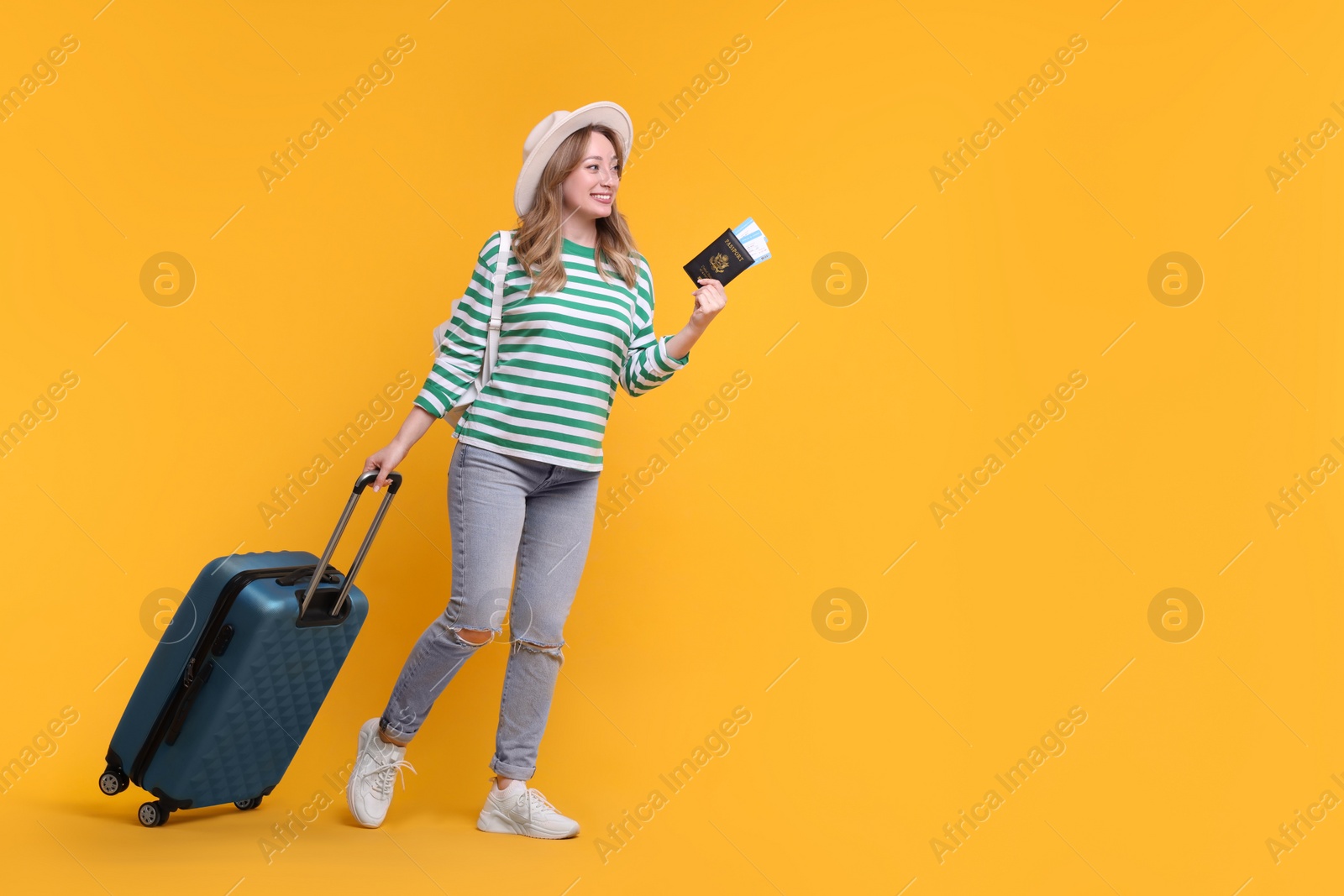 Photo of Happy young woman with passport, ticket, hat and suitcase on yellow background, space for text