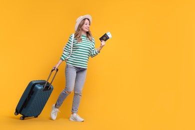 Happy young woman with passport, ticket, hat and suitcase on yellow background, space for text