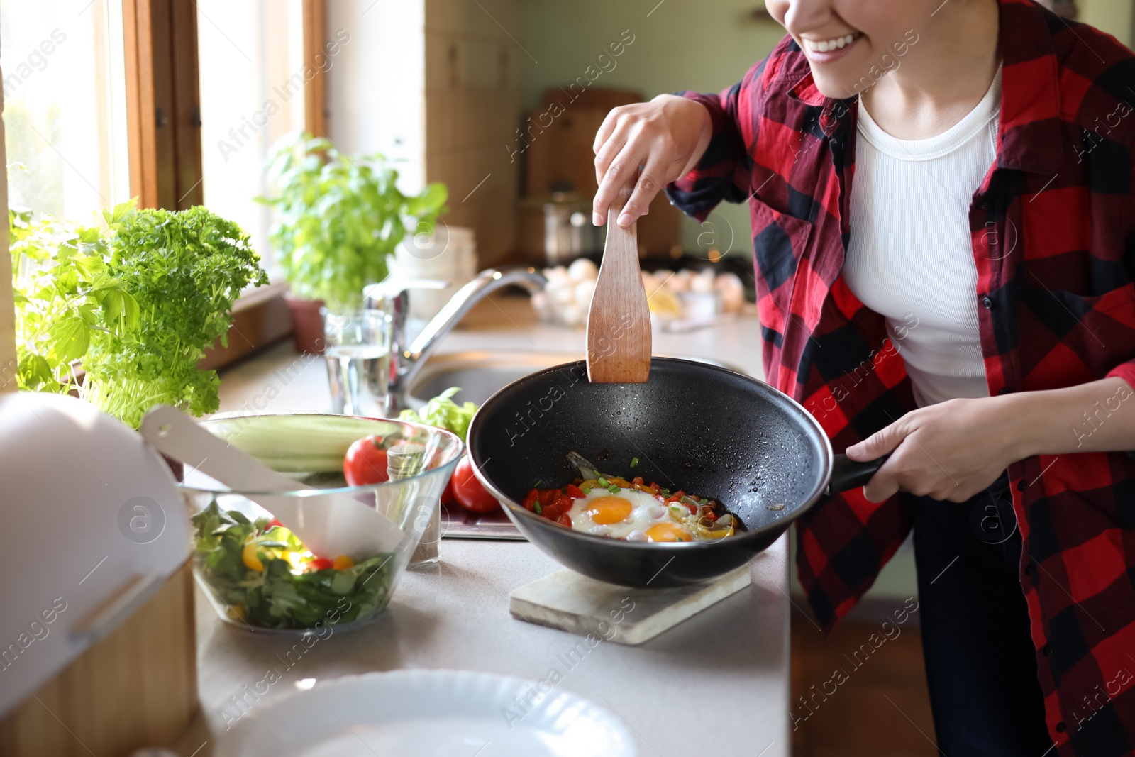 Photo of Woman holding frying pan with cooked eggs and vegetables at countertop in kitchen, closeup