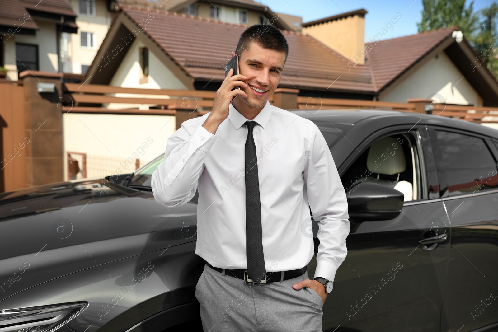 Photo of Attractive young man talking on phone near luxury car outdoors