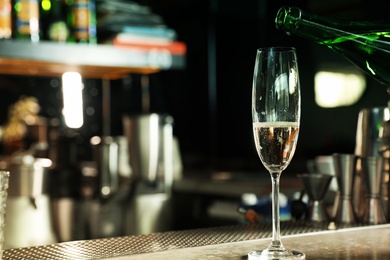 Photo of Pouring champagne from bottle into glass on counter in bar. Space for text