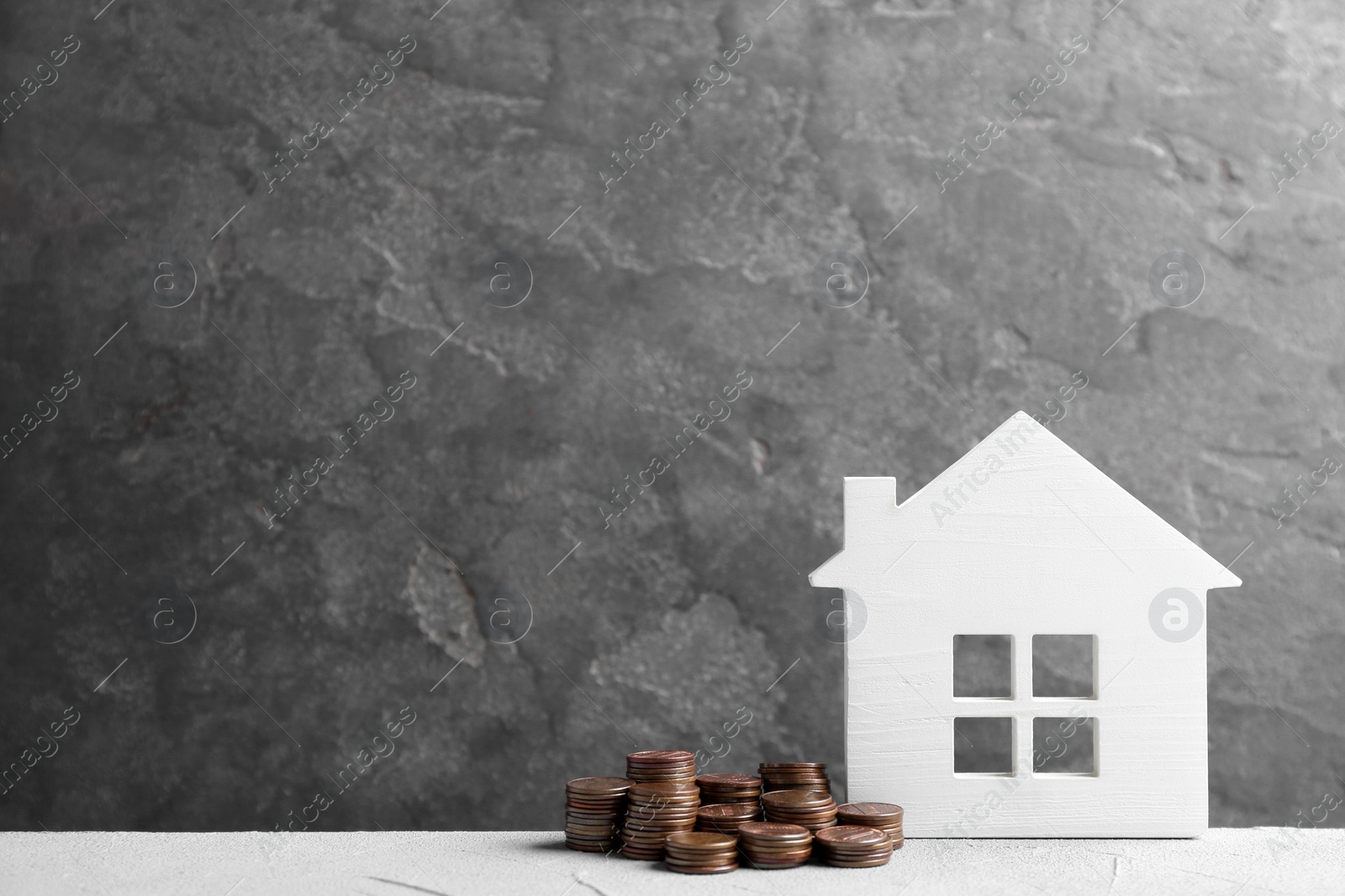 Photo of House model and coins on white table against grey background. Space for text