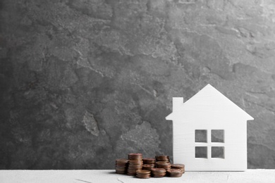 House model and coins on white table against grey background. Space for text