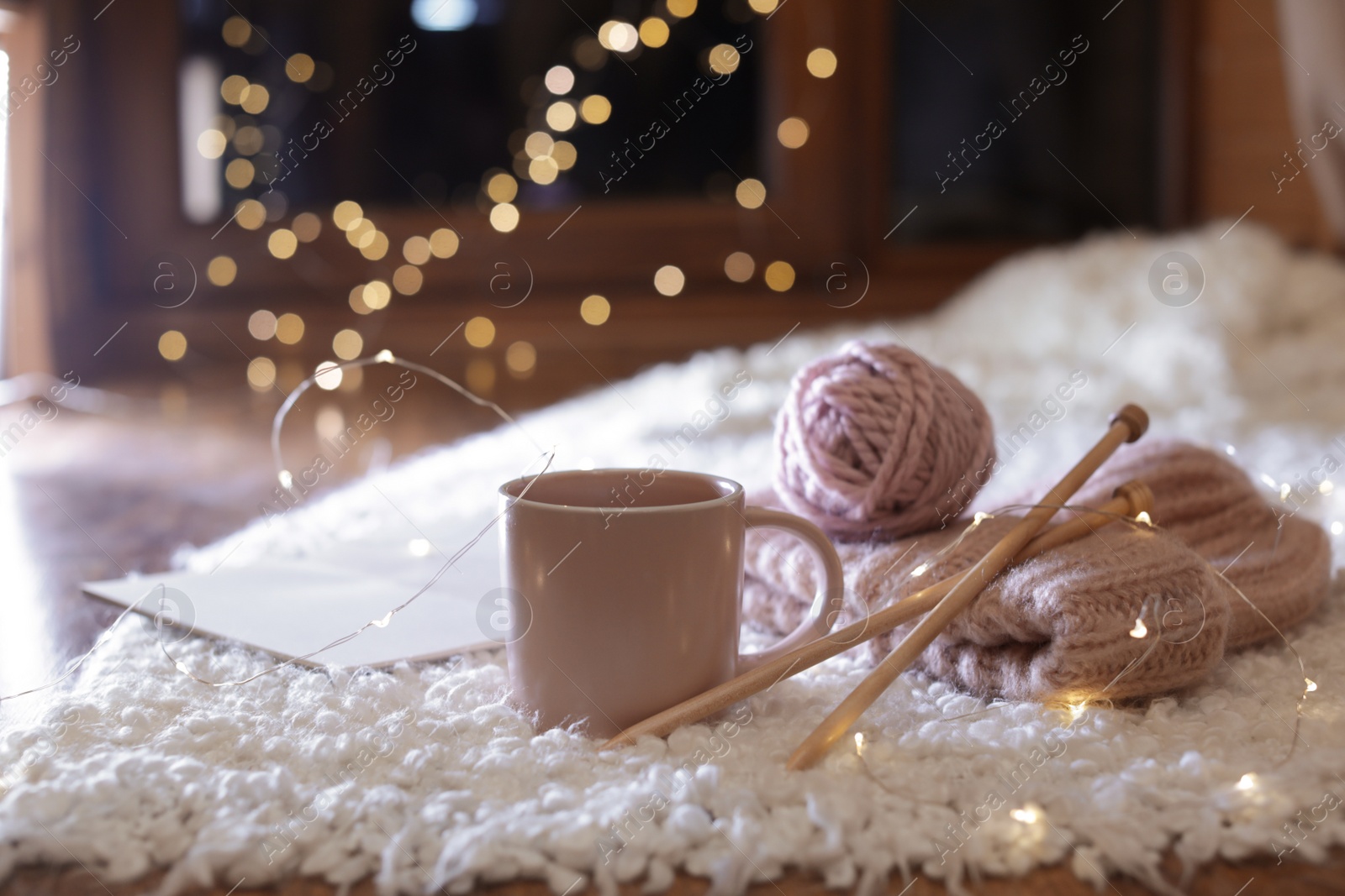 Photo of Composition with cup of hot beverage, knitting yarn and book on fuzzy rug. Winter evening