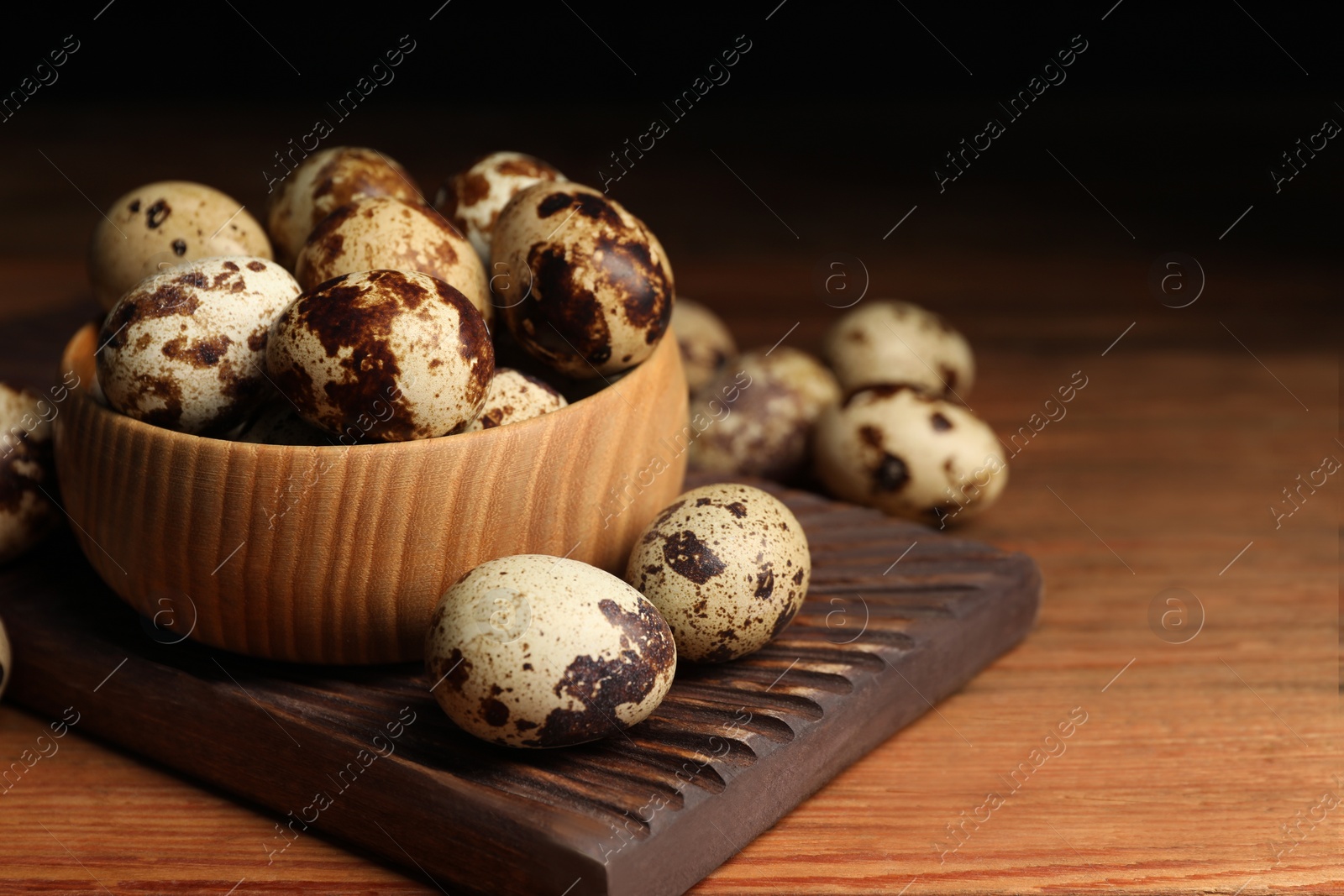 Photo of Bowl and many speckled quail eggs on wooden table. Space for text