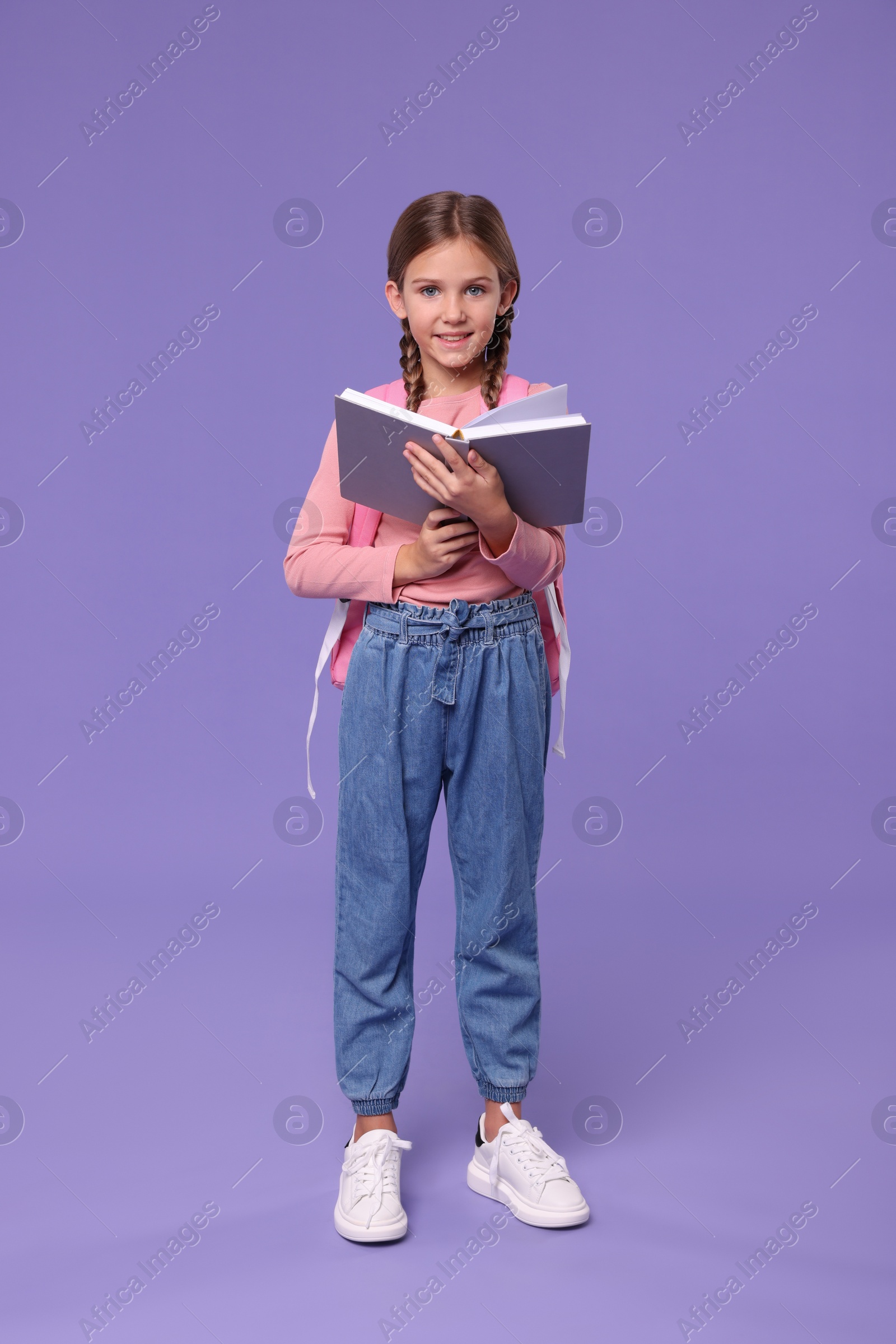 Photo of Smiling schoolgirl with open book on violet background