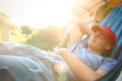 Young man resting in hammock near motorhome outdoors on sunny day