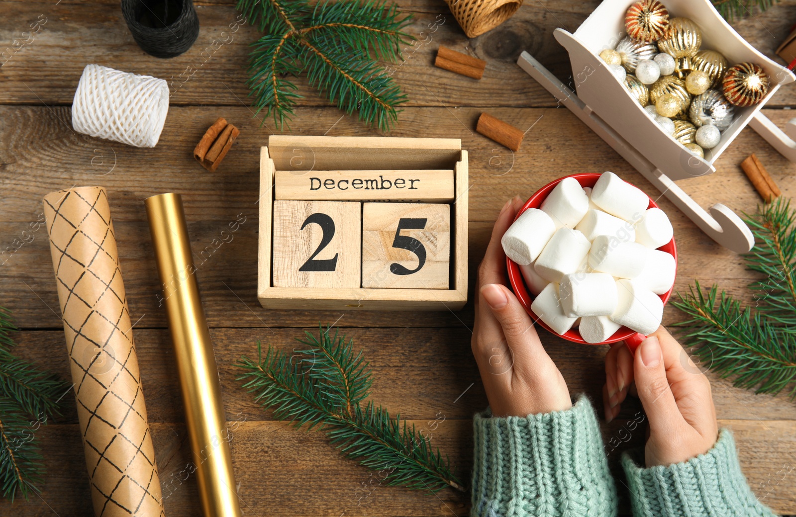 Photo of Woman holding hot drink near block calendar at wooden table, top view