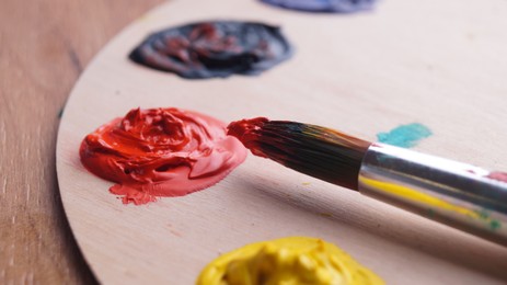 Photo of Artist's palette with colorful paints and brush on wooden table, closeup