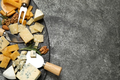 Photo of Cheese platter with specialized knives and fork on grey table, top view. Space for text