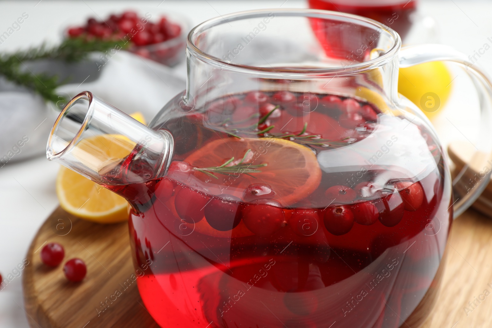 Photo of Tasty hot cranberry tea with lemon, rosemary and fresh berries in teapot on table, closeup