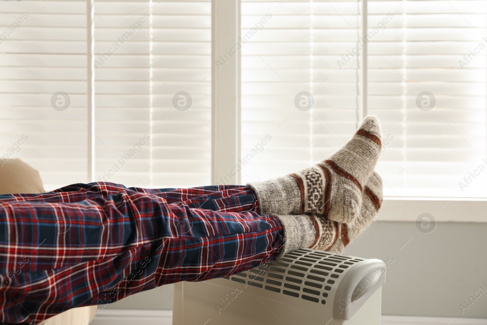 Photo of Man warming feet on electric heater at home, closeup