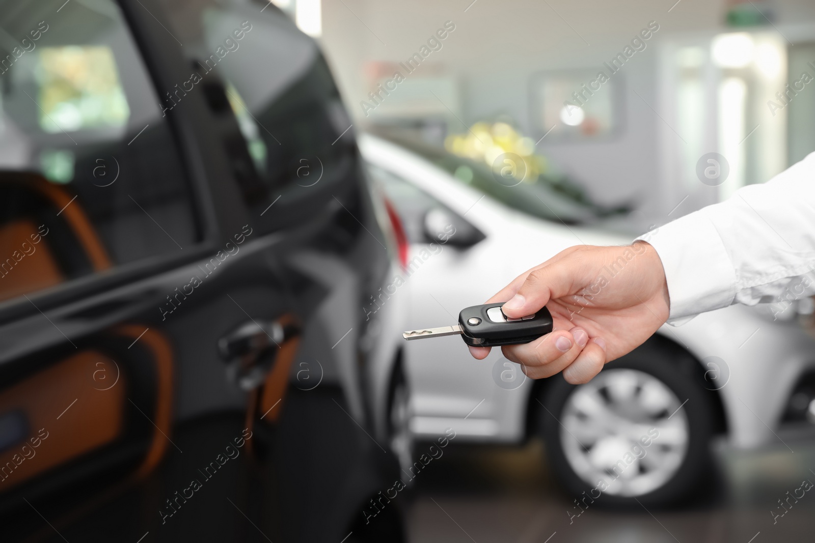 Photo of Young man turning off alarm system with car key indoors, closeup