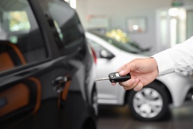 Photo of Young man turning off alarm system with car key indoors, closeup