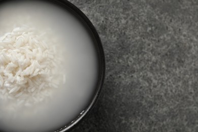 Photo of Bowl with rice soaked in water on grey table, top view. Space for text