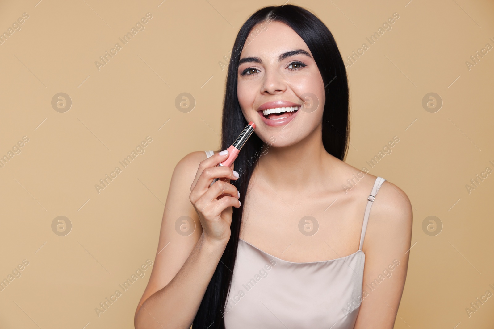 Photo of Young woman with beautiful makeup holding nude lipstick on beige background