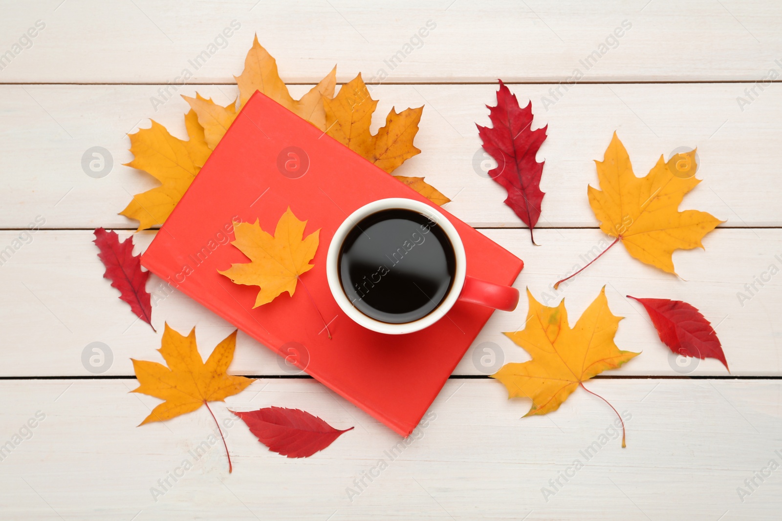 Photo of Cup of hot coffee, book and autumn leaves on white wooden table, flat lay