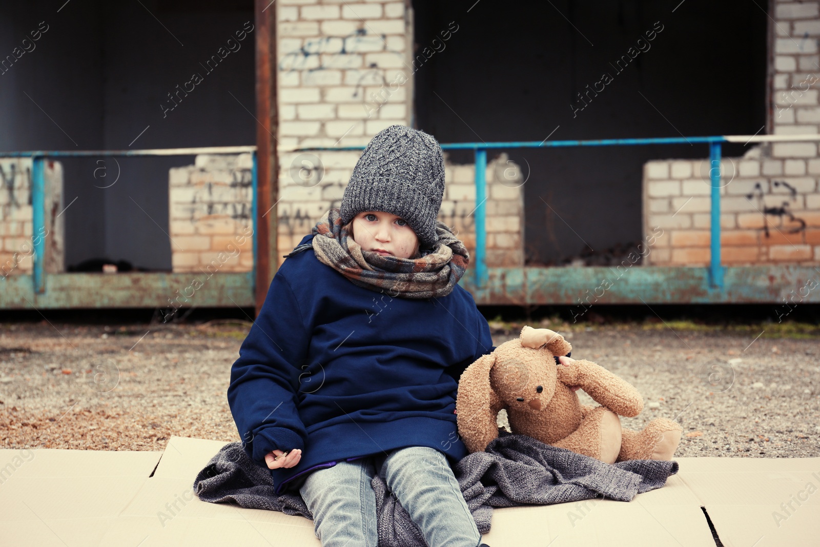 Photo of Poor little girl with toy rabbit on dirty street