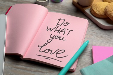 Photo of Open notebook with motivational phrase Do What You Love on wooden table