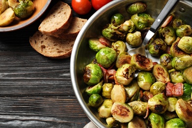 Photo of Delicious Brussels sprouts with bacon on grey wooden table, flat lay