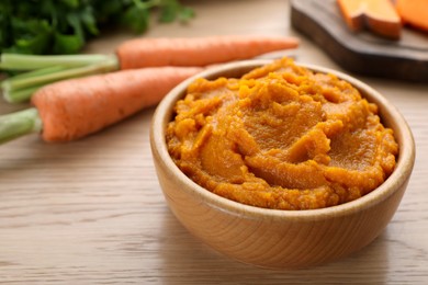 Photo of Bowl with tasty carrot puree on wooden table, closeup