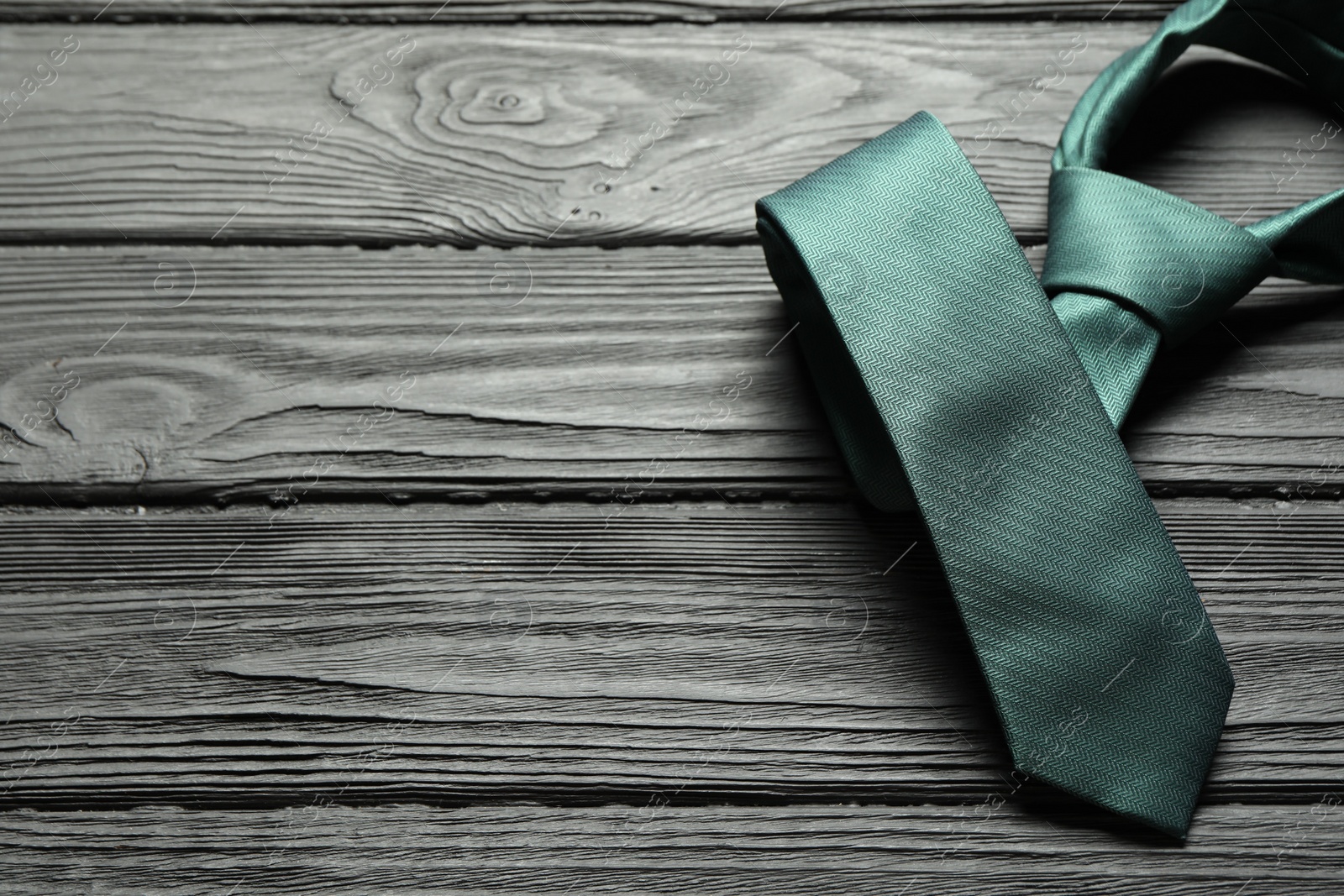 Photo of One green necktie on black wooden table, above view. Space for text