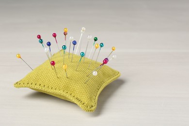 Photo of Yellow cushion with pins on white table. Space for text