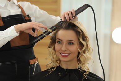 Photo of Hair styling. Hairdresser curling woman's hair in salon, closeup