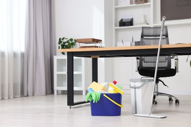 Photo of Cleaning service. Mop and bucket with supplies in office, space for text