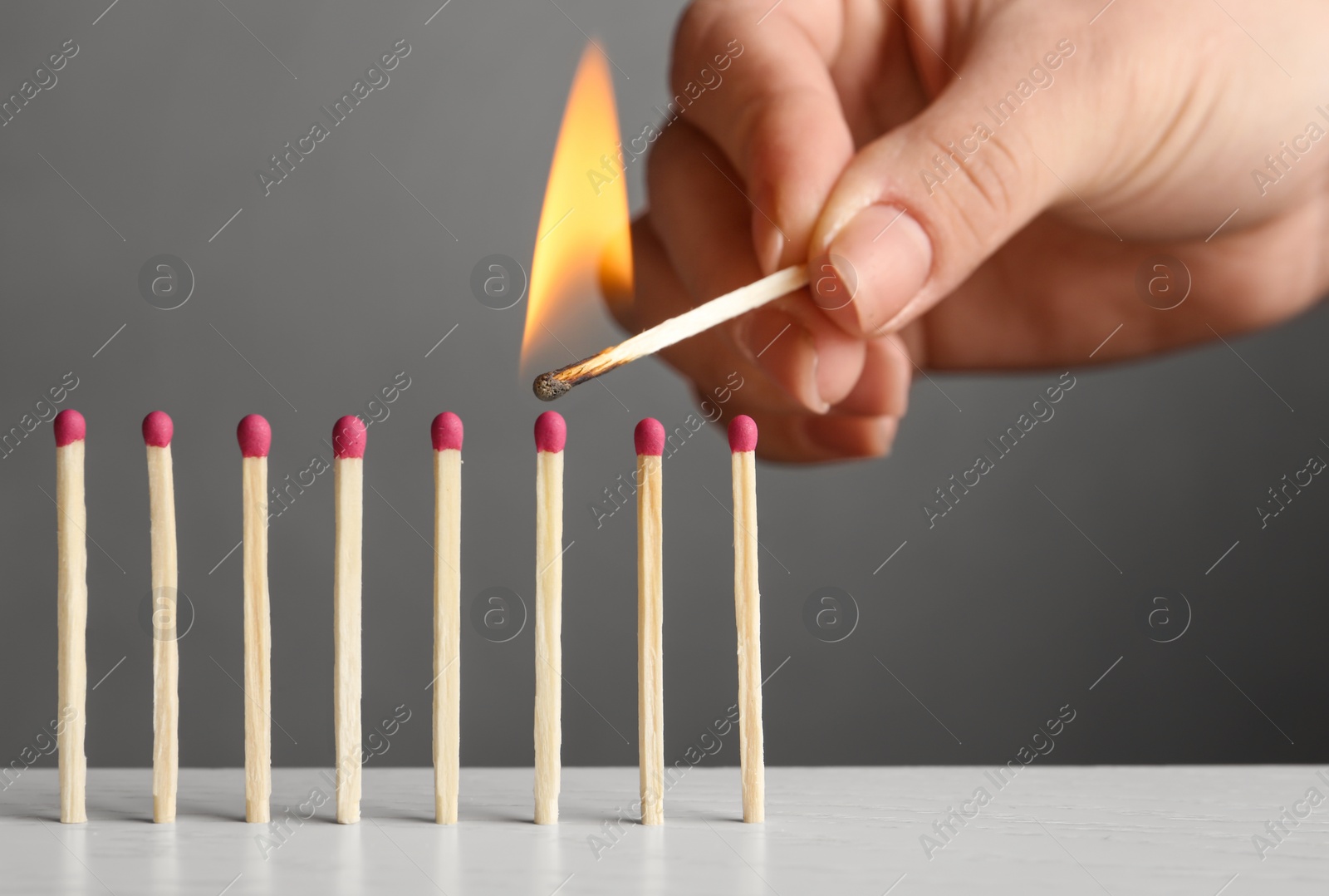 Photo of Woman igniting line of matches on table against grey background, closeup