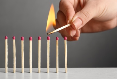 Woman igniting line of matches on table against grey background, closeup