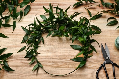 Unfinished mistletoe wreath and florist supplies on wooden table, flat lay. Traditional Christmas decor