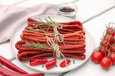 Bundles of delicious kabanosy with rosemary, peppercorn, chilli and tomatoes on white wooden table
