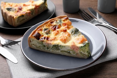 Photo of Piece of delicious homemade salmon quiche with broccoli and cutlery on wooden table, closeup