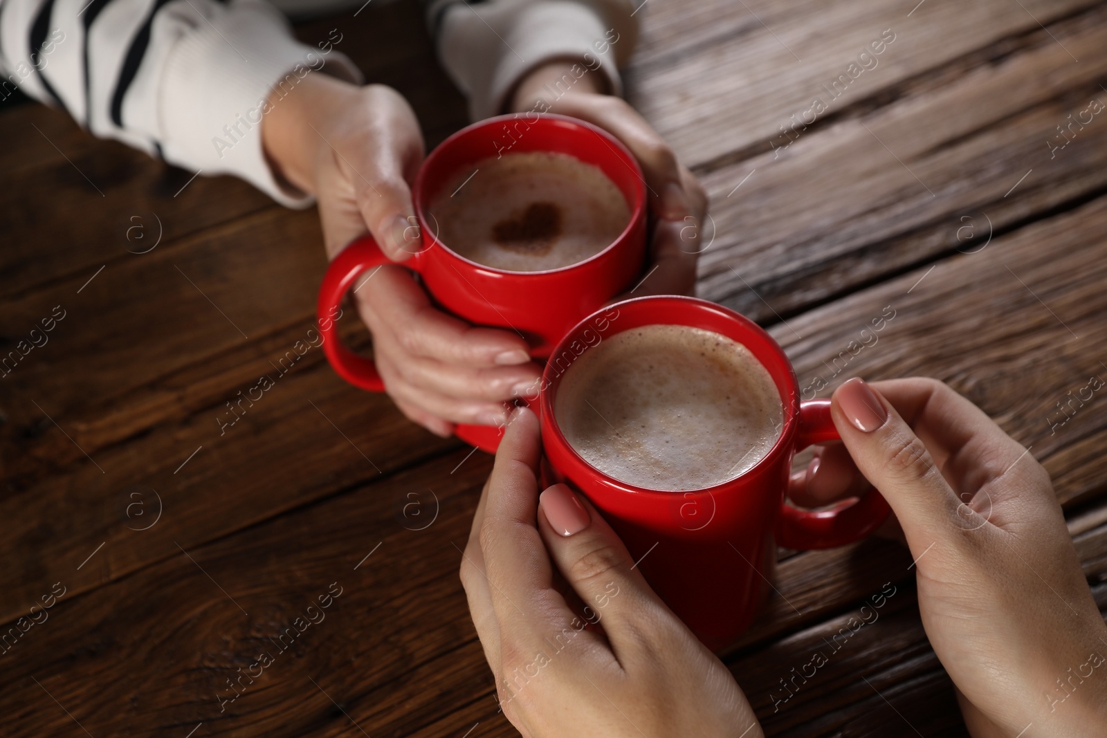 Photo of Women with mugs of hot coffee at wooden table, closeup