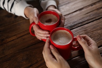 Photo of Women with mugs of hot coffee at wooden table, closeup