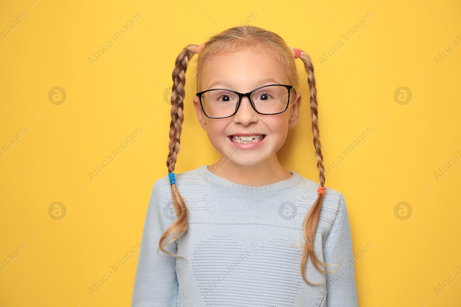 Photo of Cute little girl with braided hair and glasses on yellow background