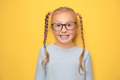 Photo of Cute little girl with braided hair and glasses on yellow background