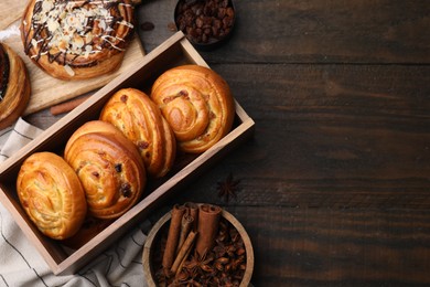 Different delicious rolls and spices on wooden table, flat lay and space for text. Sweet buns