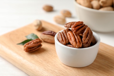 Shelled pecan nuts in bowl on wooden board. Space for text