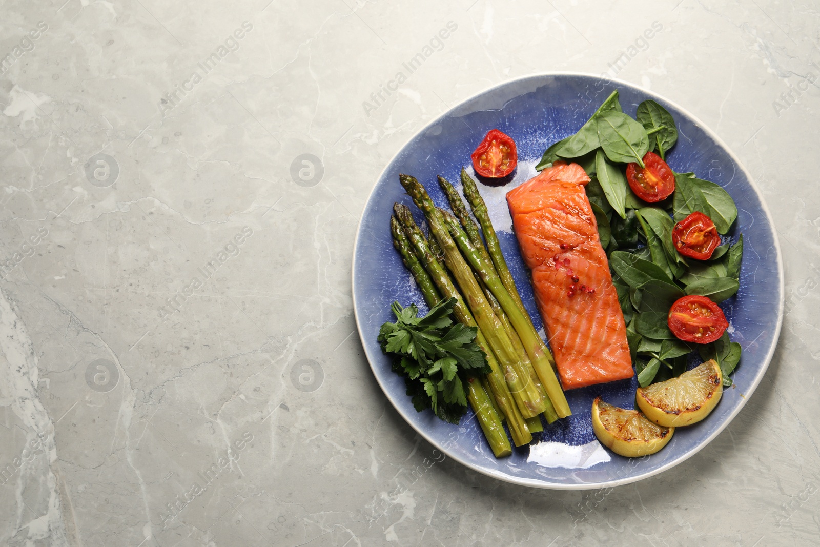 Photo of Tasty grilled salmon with tomatoes, asparagus lemon and basil on grey table, top view. Space for text